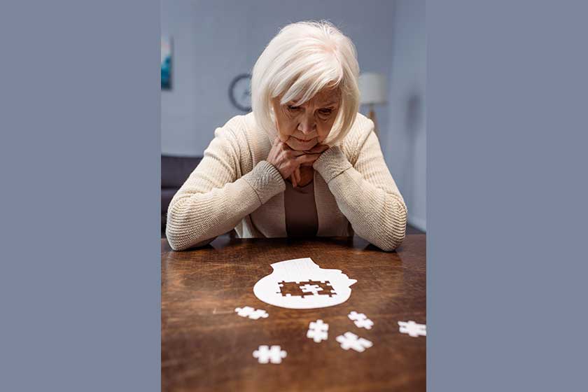 Sick senior woman thinking while collecting jigsaw puzzle