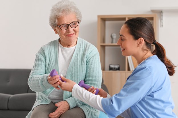 Young caregiver and senior woman training with dumbbells at home