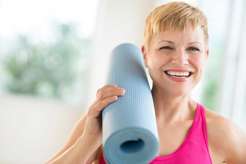 cheerful woman holding rolled up exercise mat