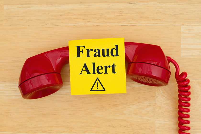 Fraud alert on sticky note with a retro red phone on textured wo Fraud alert on sticky note with a retro red phone on textured wo