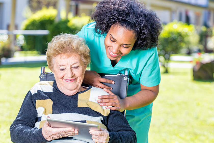 Nurse explaining tablet use to elder woman on wheelchair