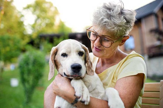 Portrait of senior woman standing outdoors in garden holding pet dog