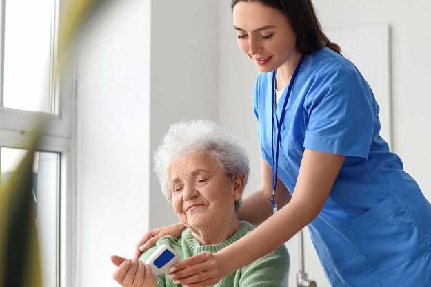 Young caregiver measuring temperature senior woman infrared thermometer kitchen Young caregiver measuring temperature senior woman infrared thermometer kitchen