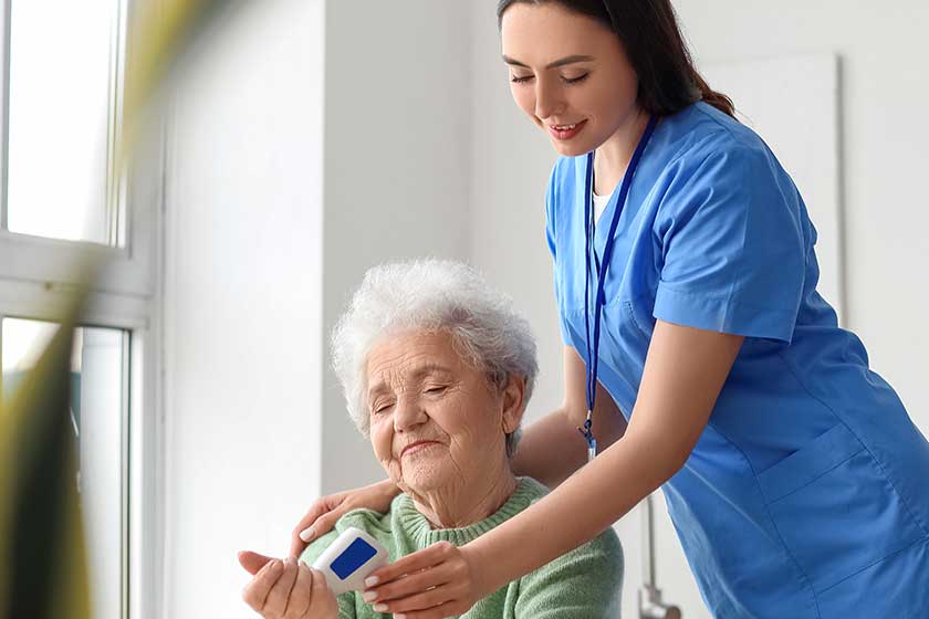 Young caregiver measuring temperature senior woman infrared thermometer kitchen