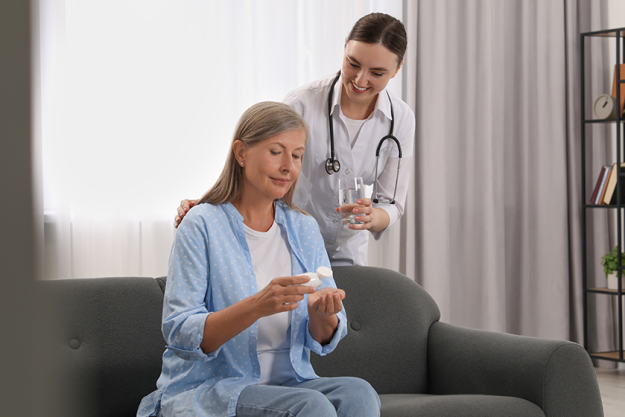 Young healthcare worker giving glass of water to senior woman with pills