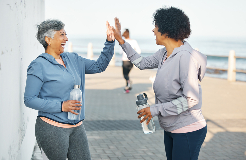 Fitness, happy and women high five by ocean for healthy lifestyle, wellness and cardio on promenade. Sports, friends and female people celebrate on boardwalk for exercise, training and workout goals
