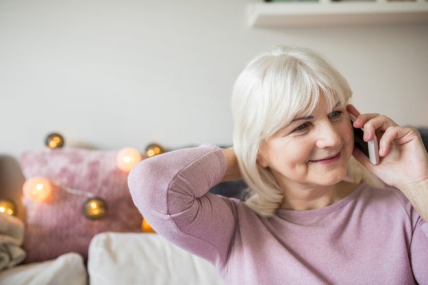 Glad senior lady talking on mobile sitting at home How We Support Your Parents With Dementia As They Live Alone In Our Memory Care Home In Houston, TX