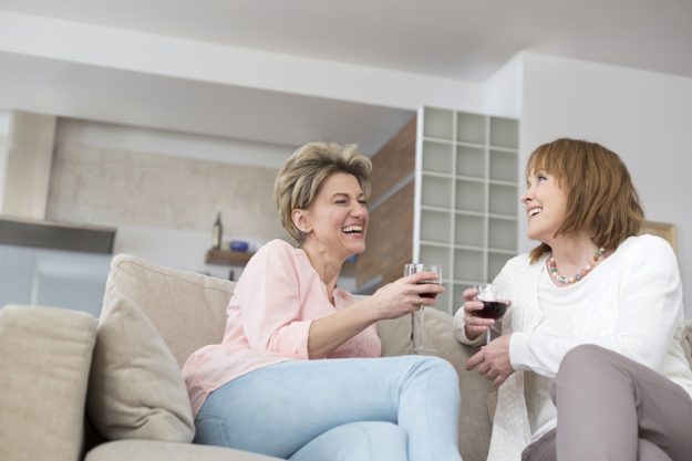 Cheerful mature friends with wineglasses sitting on sofa at home Cheerful mature friends with wineglasses sitting on sofa at home