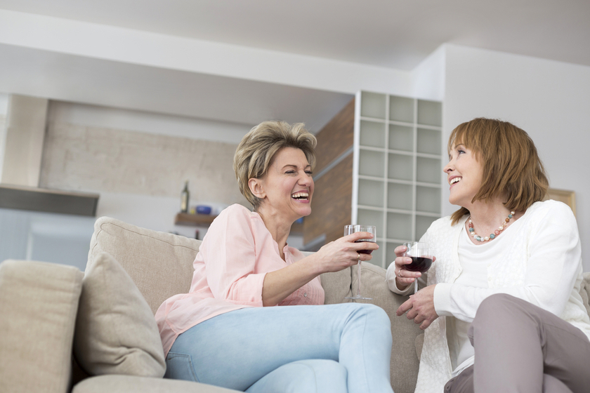 Cheerful mature friends with wineglasses sitting on sofa at home