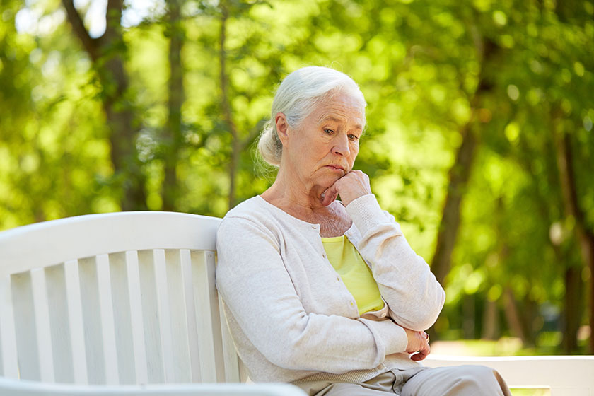 sad senior woman sitting on bench at summer park