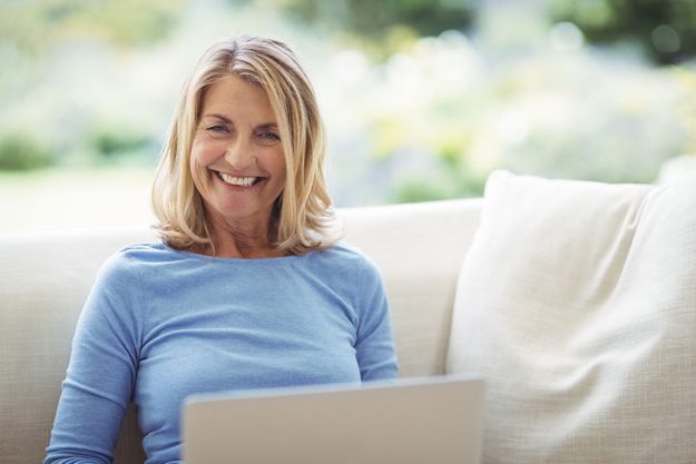 Smiling senior woman sitting on sofa with laptop Smiling senior woman sitting on sofa with laptop