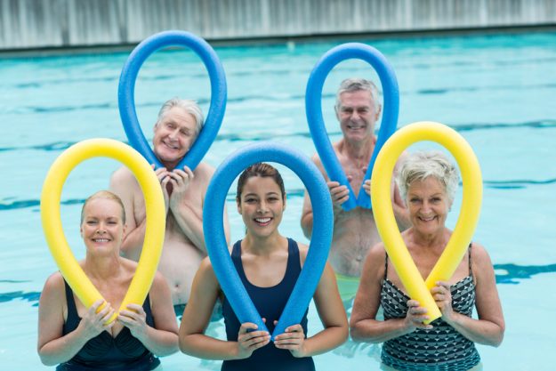 Female trainer and senior swimmers holding pool noodles Understanding Recovery Stages Of Stroke Patients