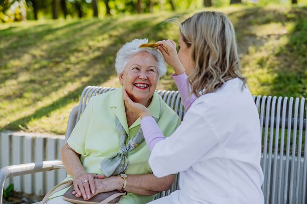 A caregiver helping senior woman to comb hair