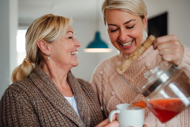 A young woman with senior mother at home pouring tea