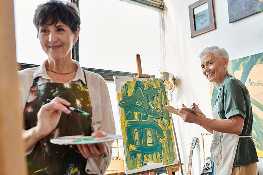 Happy mature woman palette looking female friend painting art workshop