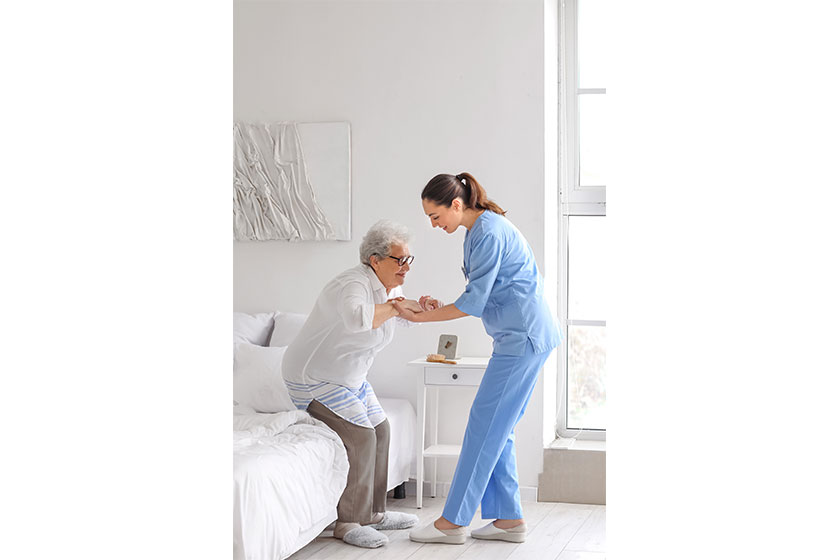 Young caregiver helping senior woman stick stand bedroom Young caregiver helping senior woman stick stand bedroom