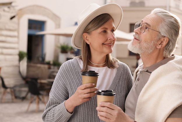 Affectionate senior couple coffee walking outdoors space text Affectionate senior couple coffee walking outdoors space text