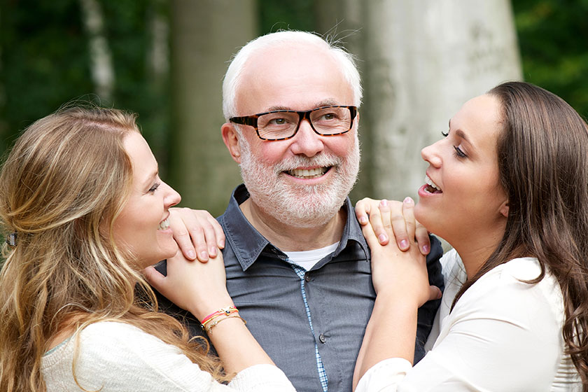 father smiling with his two daughters outdoors