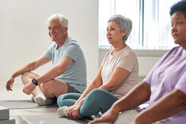 Group people sitting exercise mats exercising together yoga studio
