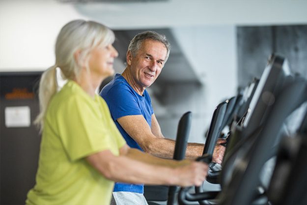 happy senior couple training on stair stepper at gym
