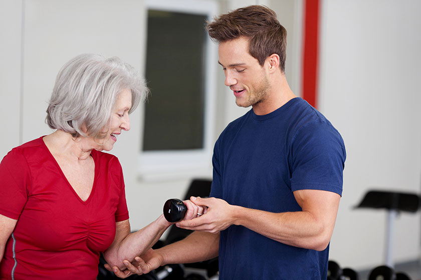 Personal Trainer For Seniors How To Find The Right Fit For Your   Male Gym Trainer Instructing An Elderly Woman 