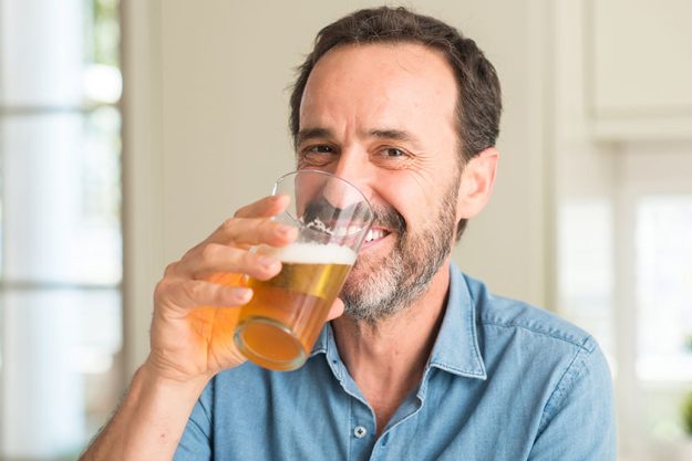 Middle age man drinking beer happy face standing smiling confident
