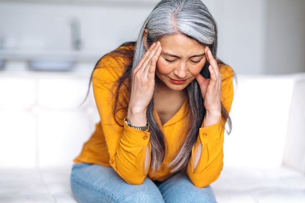 Middle aged gray haired asian woman sits couch living room