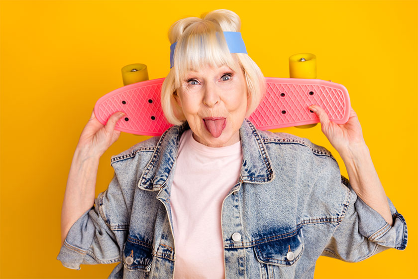 photo portrait of elder woman keeping skateboard showing tongue feel young isolated on bright yellow
