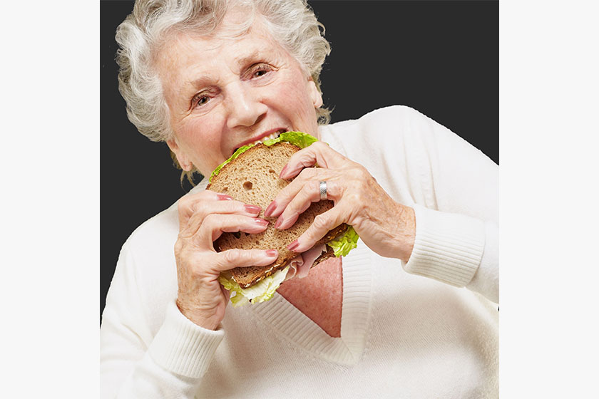 Portrait of senior woman eating vegetal sandwich over black back