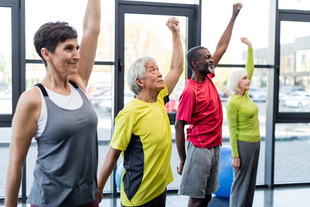 grey haired asian man training multiethnic people gym