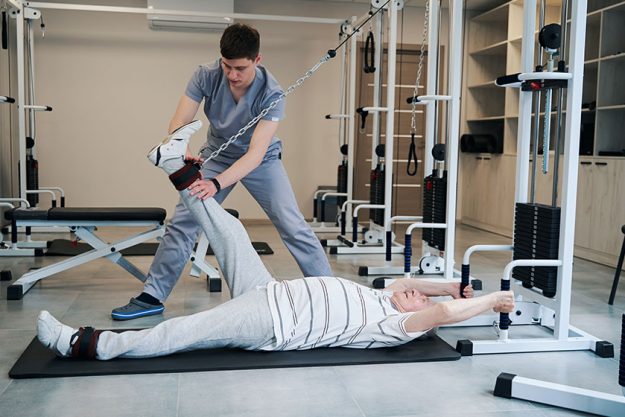 lying pensioner doing exercise on cable pulley weight training system