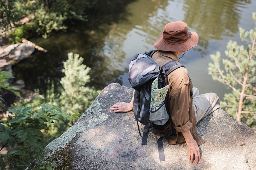 senior woman backpack map sitting rock lake