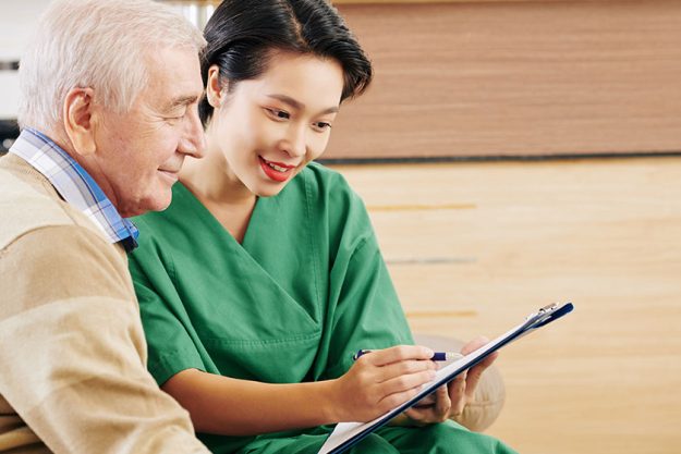 Young Vietnamese retiment home volunteer showing senior man results his