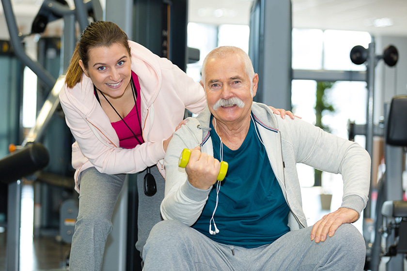 female trainer assisting senior man lifting dumbbells gym female trainer assisting senior man lifting dumbbells gym