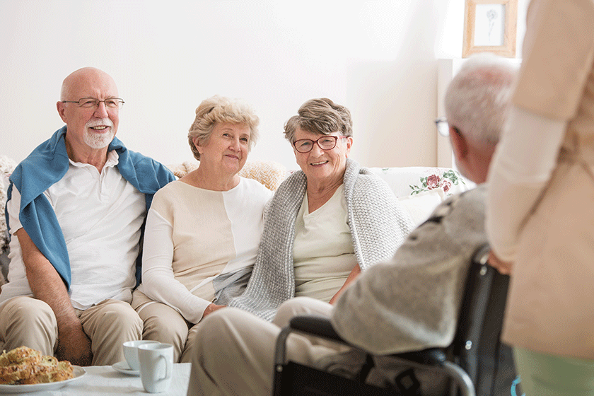 group of senior friends sitting together in common living room of nursing home