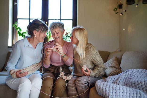 happy senior women friends having fun knitting together indoors at home