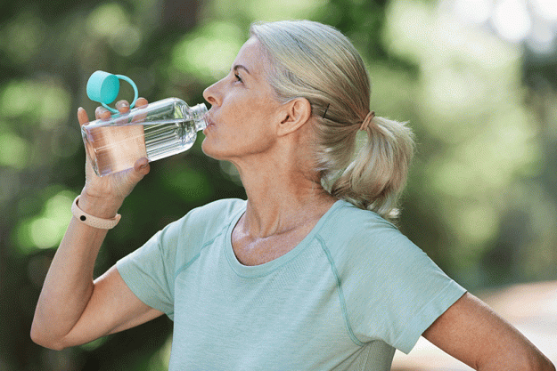 shot mature woman drinking water while exercising outdoors
