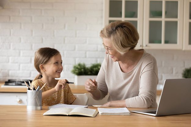 Smiling grandmother help granddaughter with homework assignment