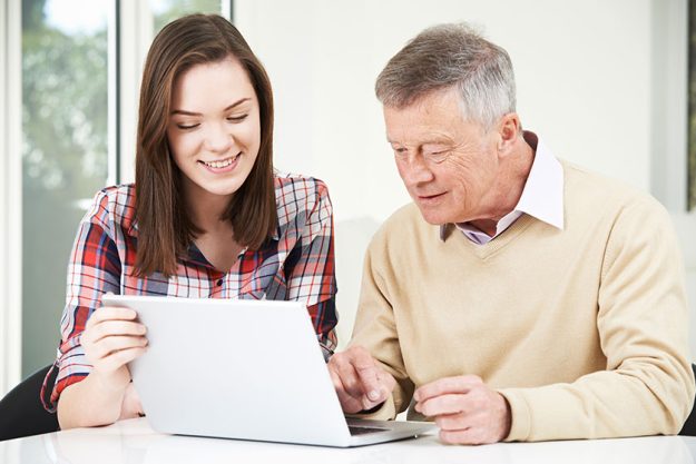 teenage granddaughter showing grandfather how to use laptop comp