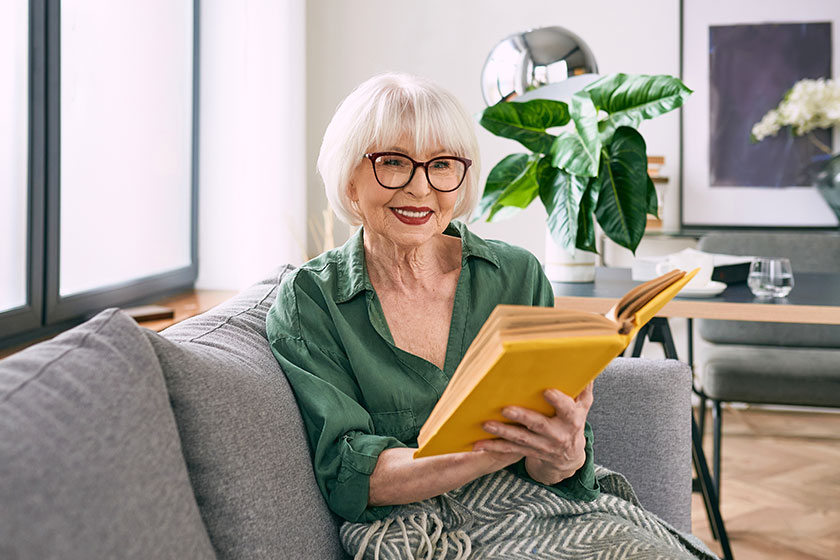 cheerful senior woman sitting couch reading book home education mature