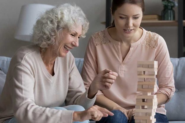 laughing mature mother play in tumbling tower with grown daughter