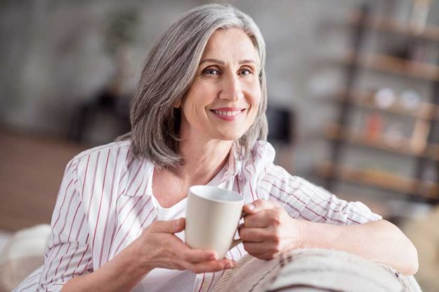 photo of happy cheerful positive old lady good mood hold hands mug weekend indoors inside