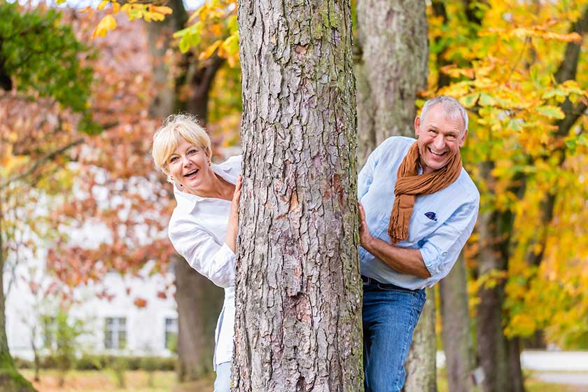 senior couple flirting playing around tree in park senior couple flirting playing around tree in park