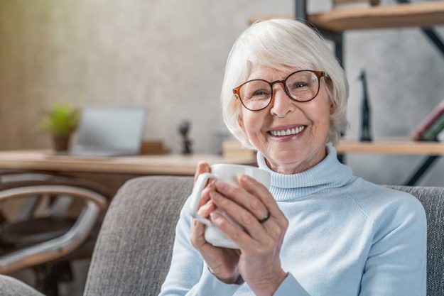 senior woman drinking hot drink sitting sofa home