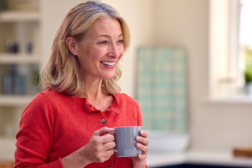 smiling mature woman standing kitchen relaxing cup coffee