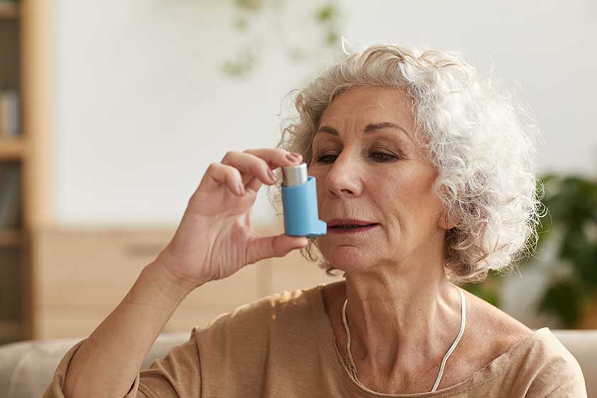warm toned head shoulders portrait portrait senior woman using inhaler