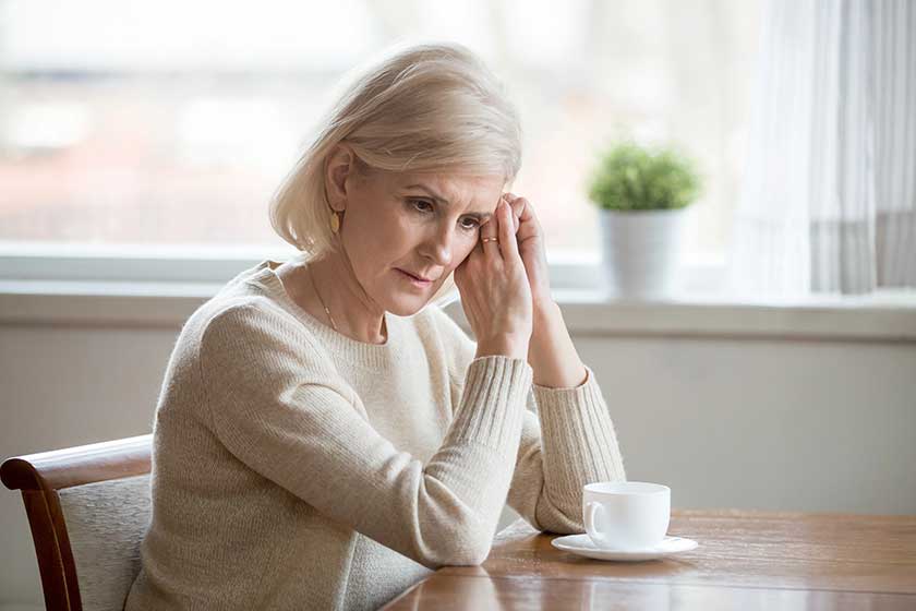 concerned aged woman sit at table lost in thoughts