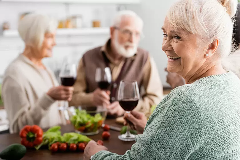 happy senior woman holding glass red wine retired friends blurred