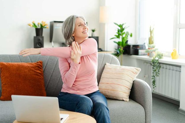 smiling active senior woman stretching arms doing exercises sitting comfortable