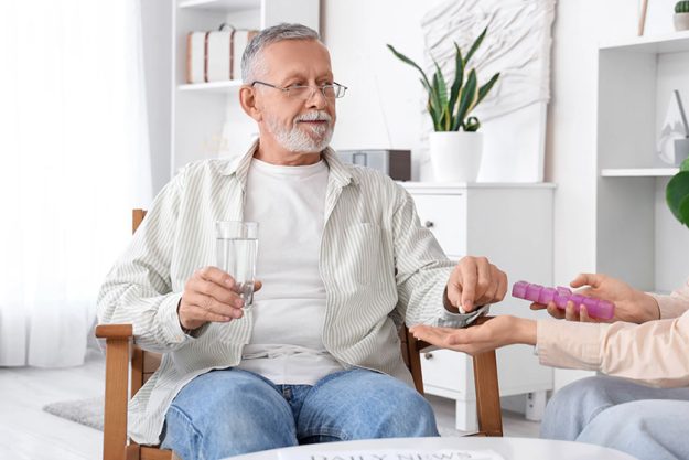 Senior man glass water taking pill caregiver nursing home
